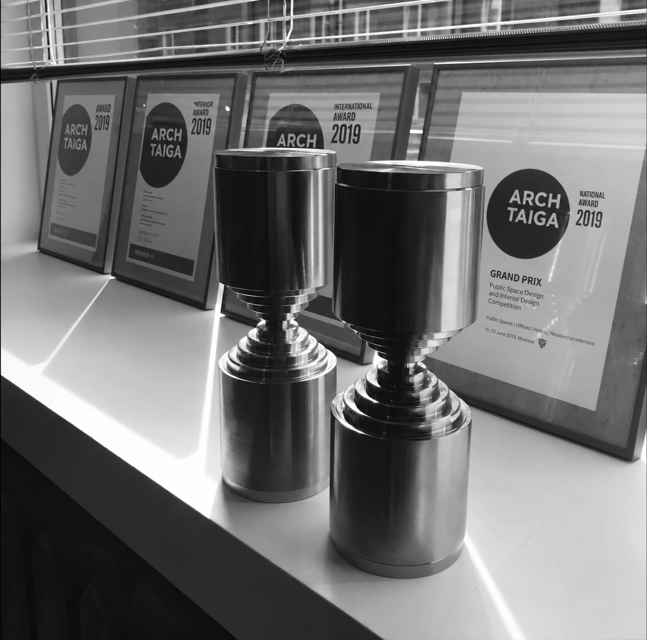 Two metal ARCH TAIGA trophies on a windowsill in front of framed 2019 award certificates