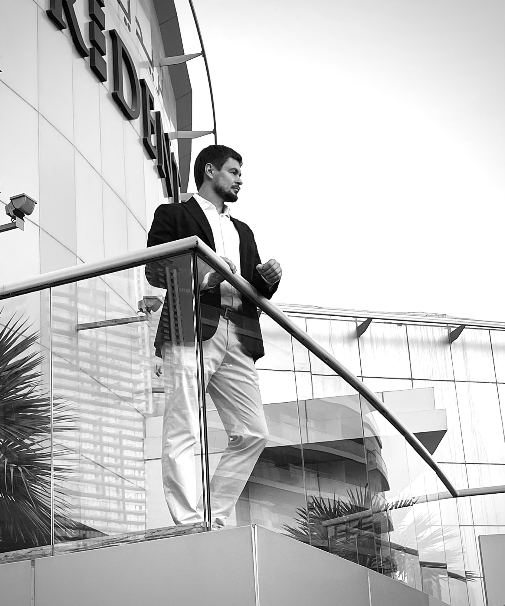 Roman Chertkov in a jacket on a terrace with a glass railing in front of a curved facade