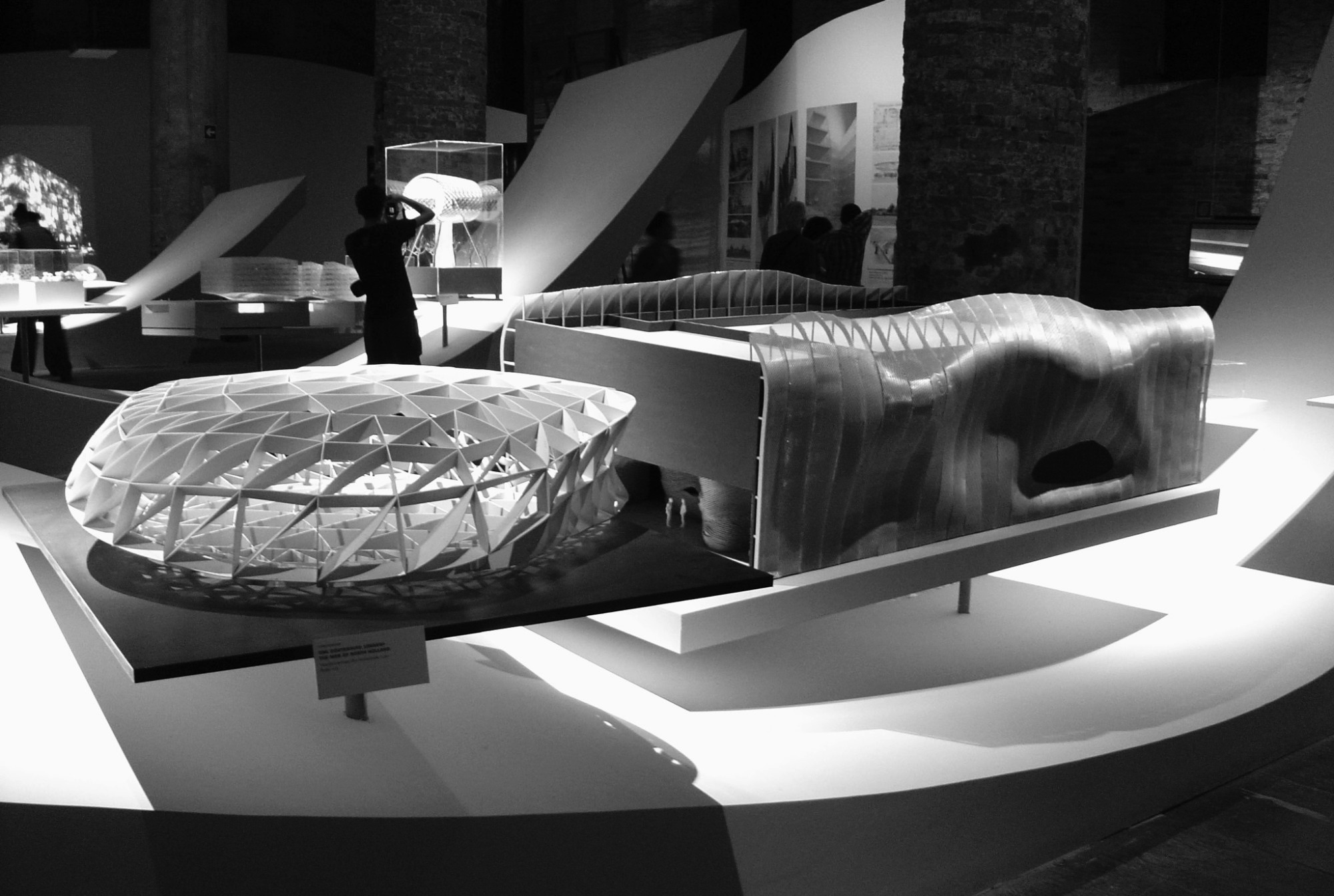 Architectural models on white plinths in a brick hall