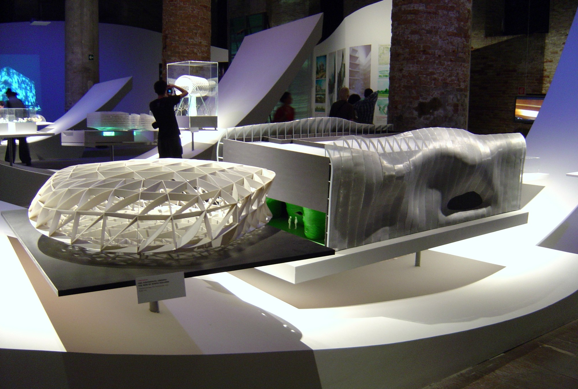 Architectural models on white plinths in a brick hall