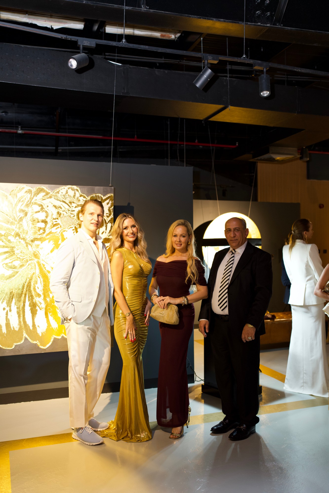 Four guests posing in front of a gold floral painting