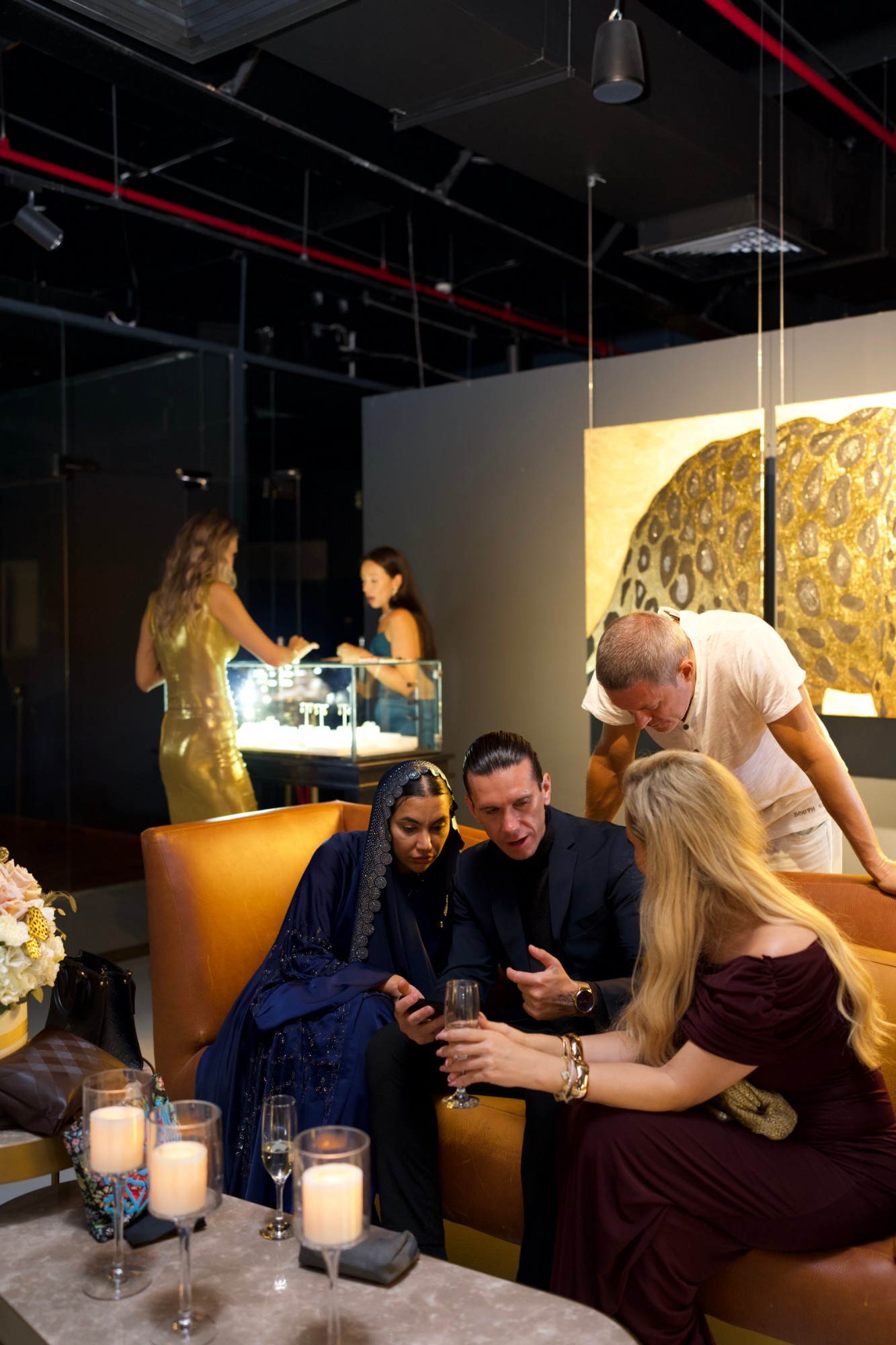 Guests on a leather sofa looking at a phone, jewellery vitrine behind