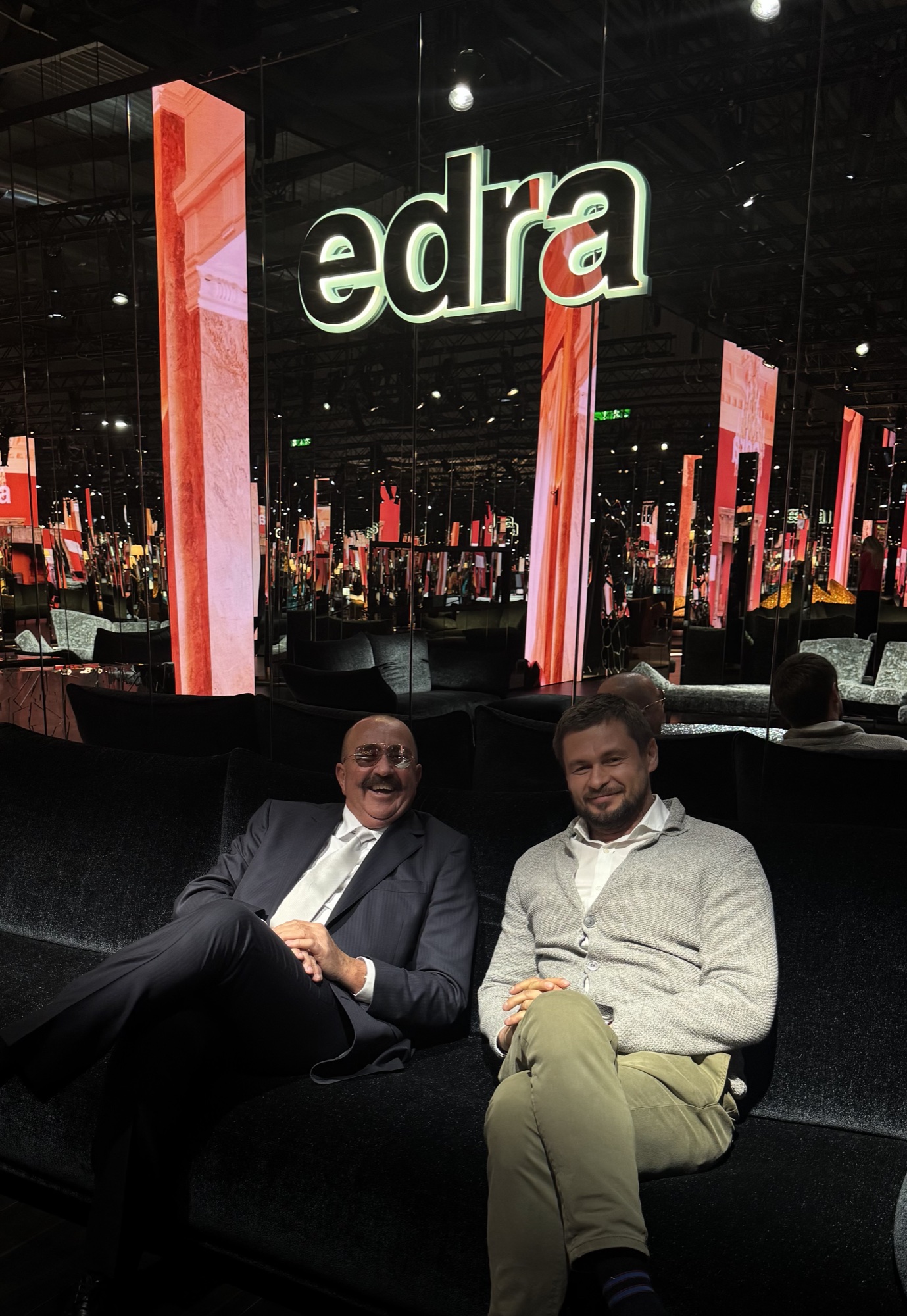 Roman Chertkov and a companion on a sofa under the Edra sign at Salone del Mobile