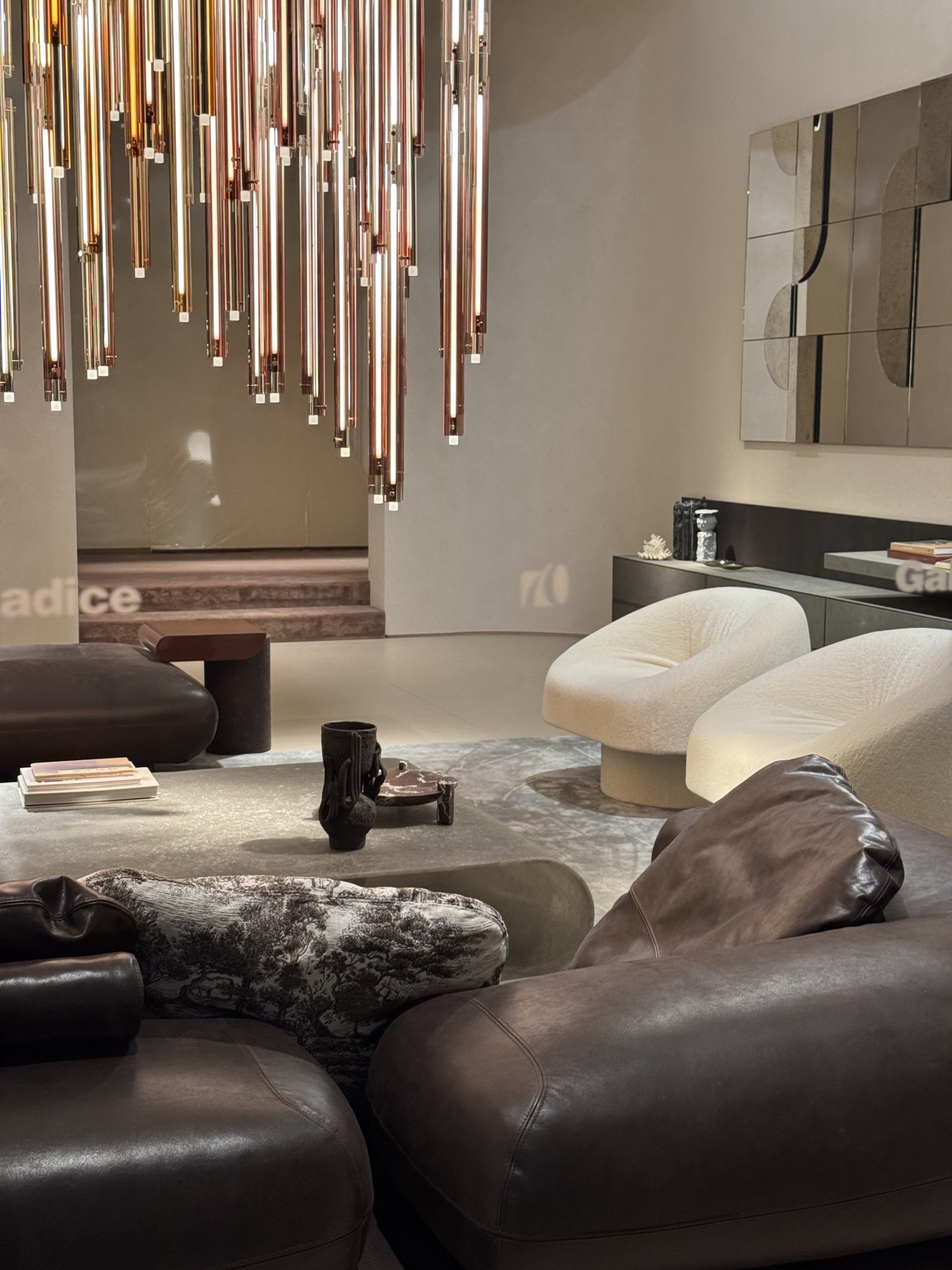 Showroom with a chandelier of brass rods above leather armchairs