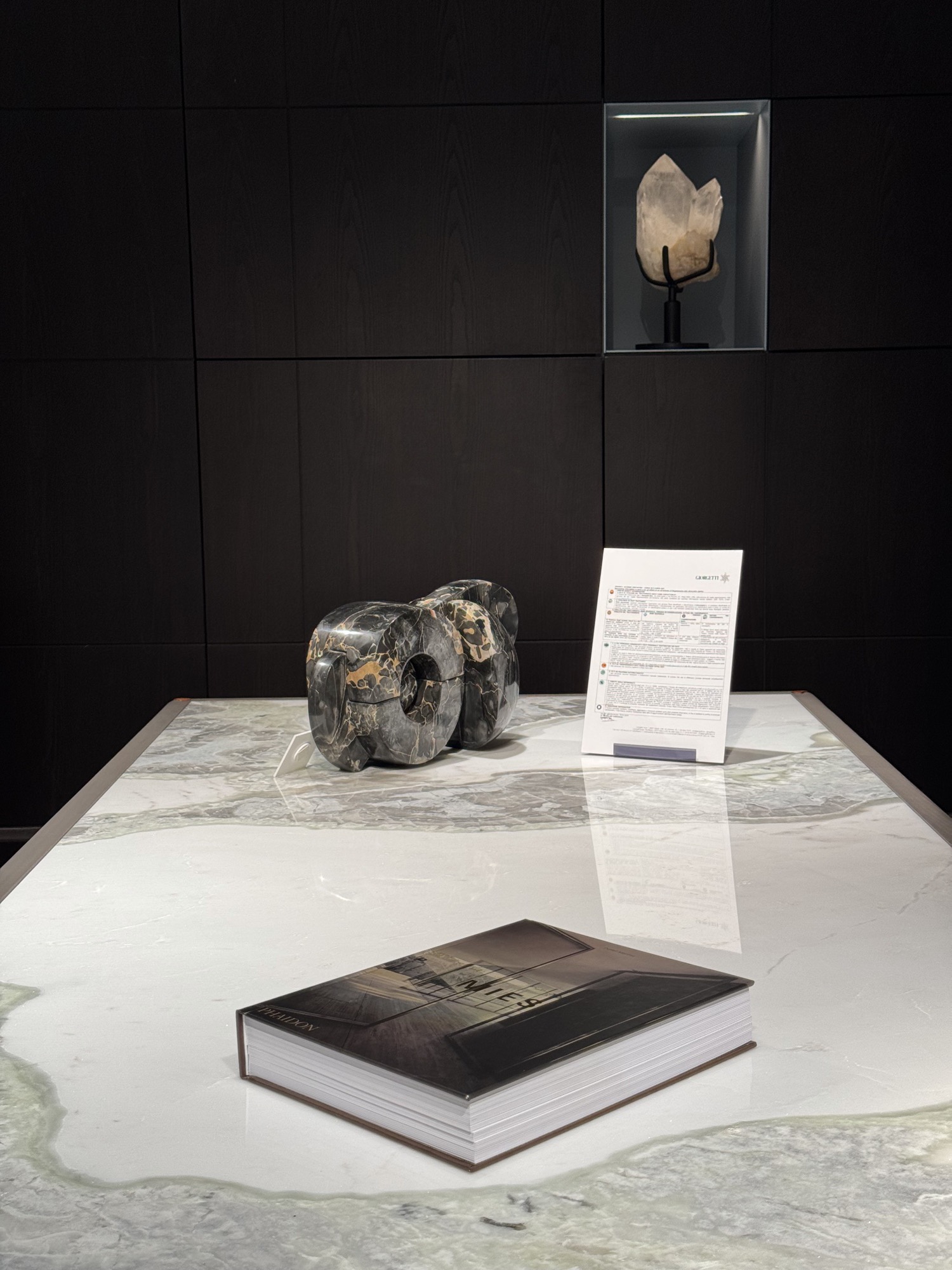 Sculptural stone object and a book on a marble table in a dark showroom