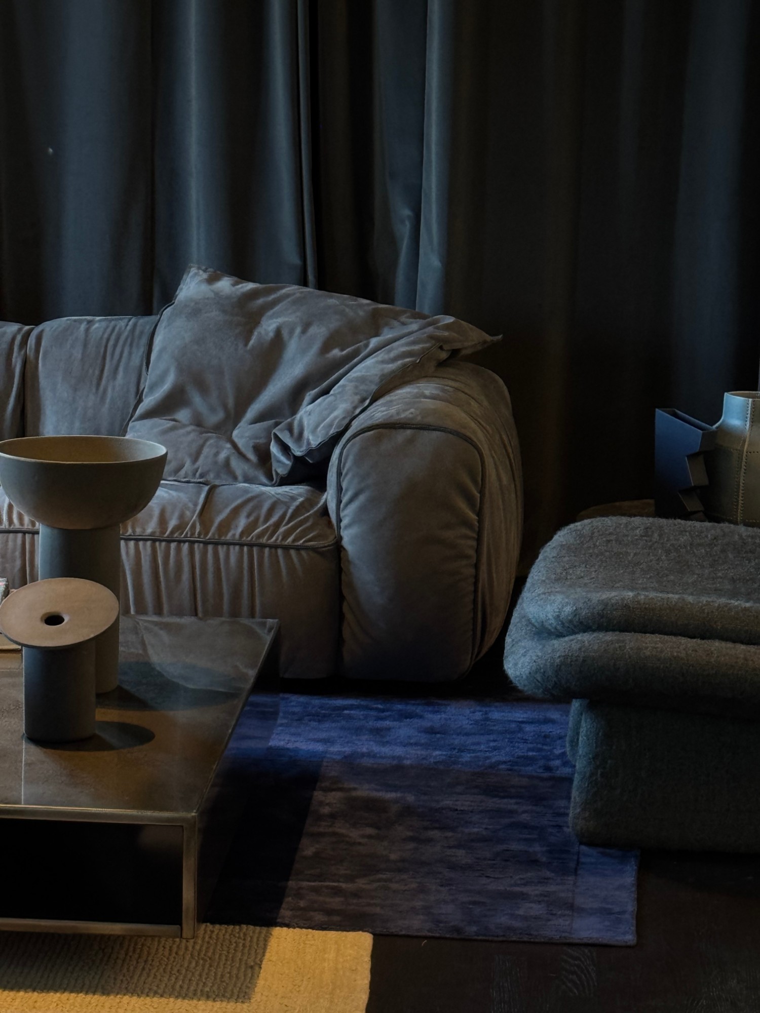 Dark showroom vignette with a suede sofa and a blue rug