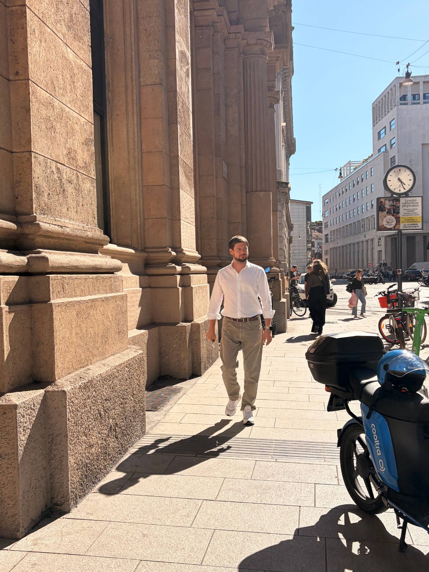 Roman Chertkov walking past a stone colonnade on a sunny Milan street