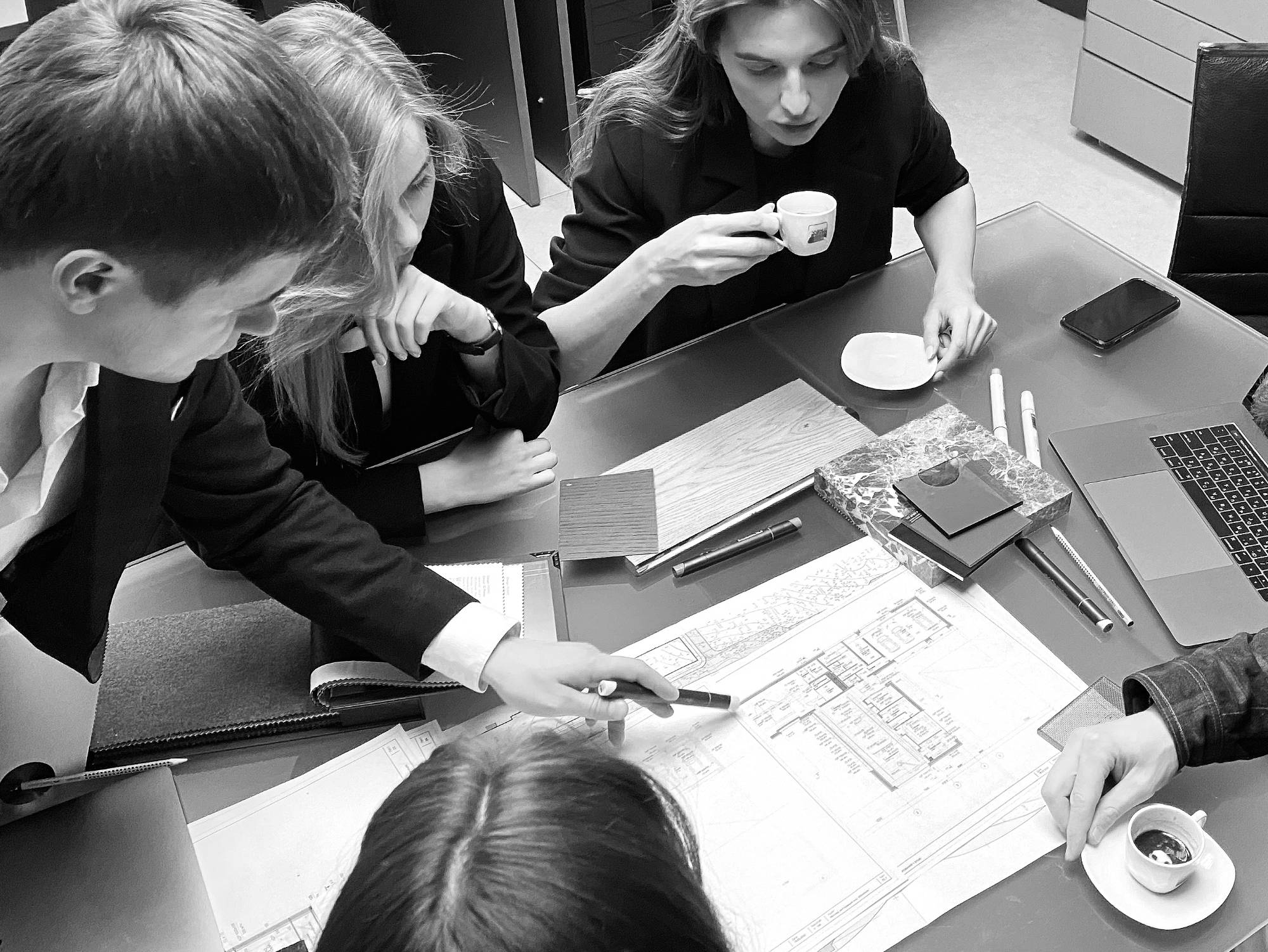 Team around a table with drawings and material samples, one person pointing with a pen