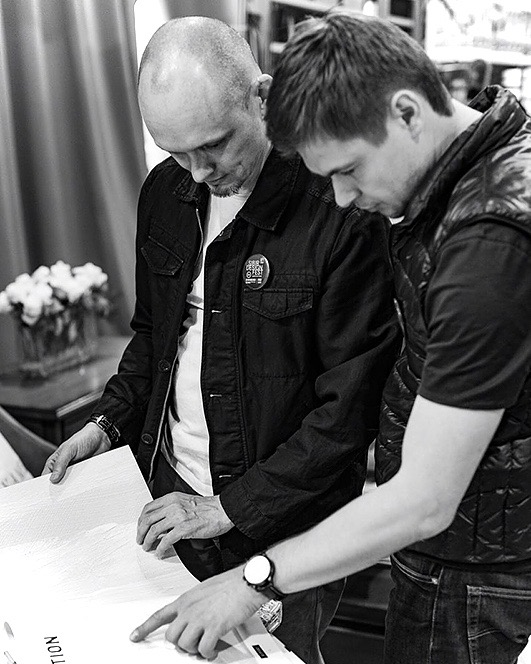 Two men bending over drawings on a table, one pointing at a sheet