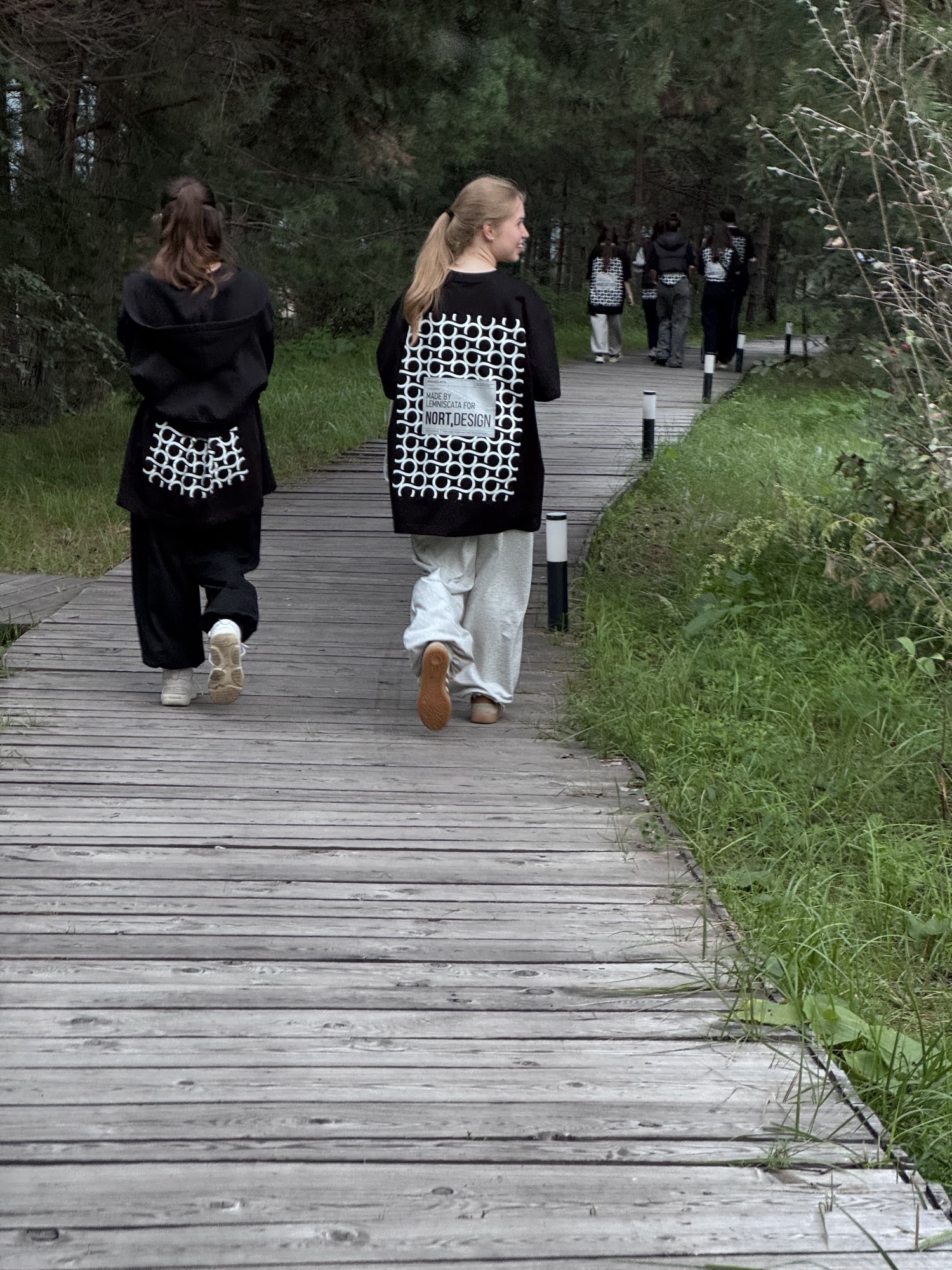 Team members walking along a wooden boardwalk through the forest with NORT.DESIGN tote bags