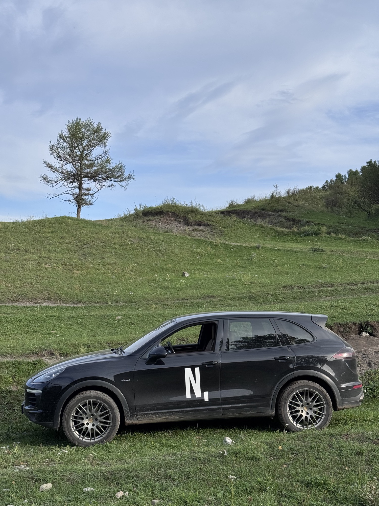 Black SUV with an N. logo on the door parked on a green hillside