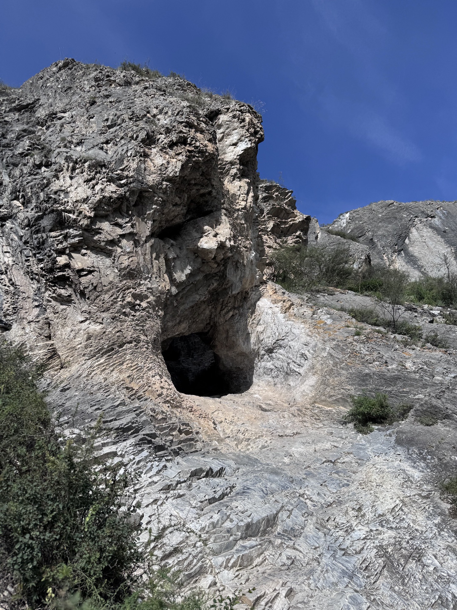 Cave opening in a grey rock face under a blue sky