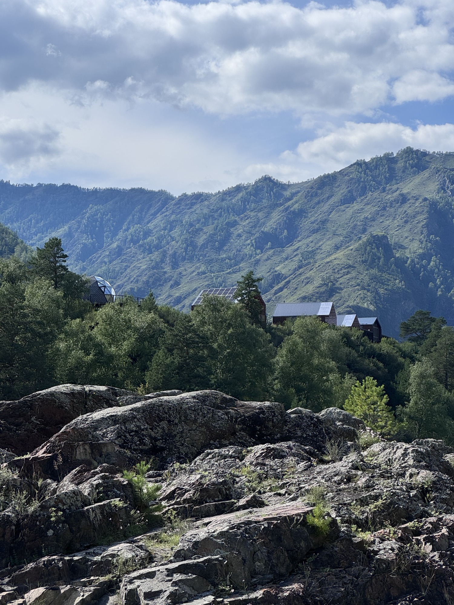 Rocky outcrop, forest and glamping domes against a mountain ridge