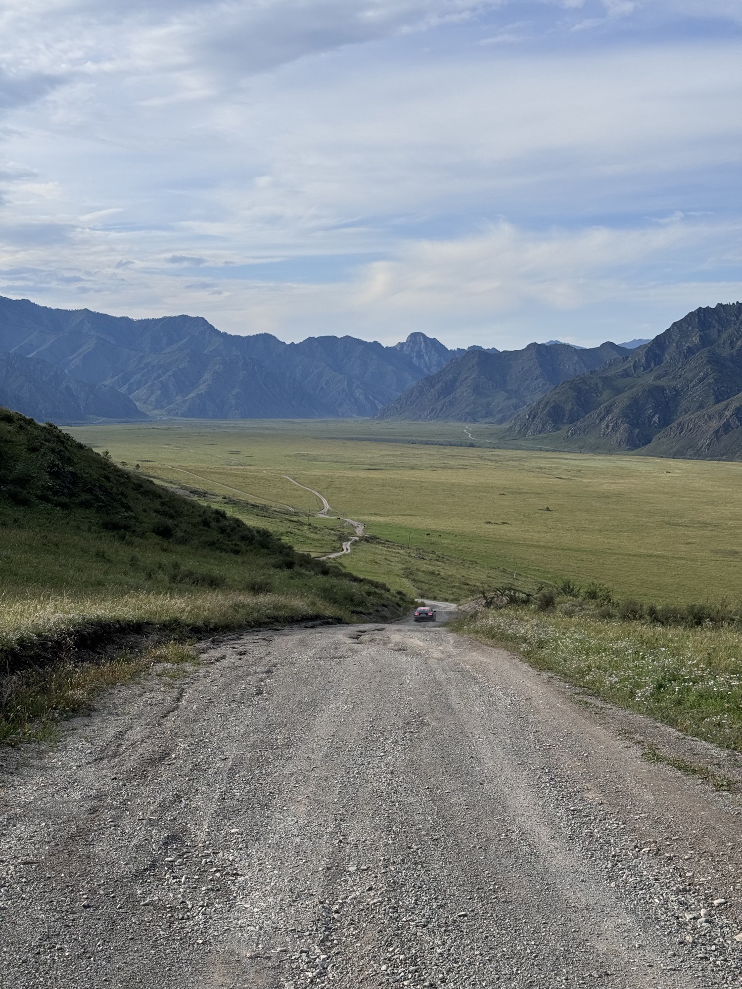Gravel road descending into a wide valley between mountains