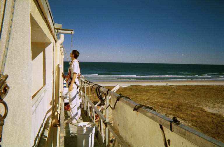 Young Roman in a safety harness on a building facade by the ocean